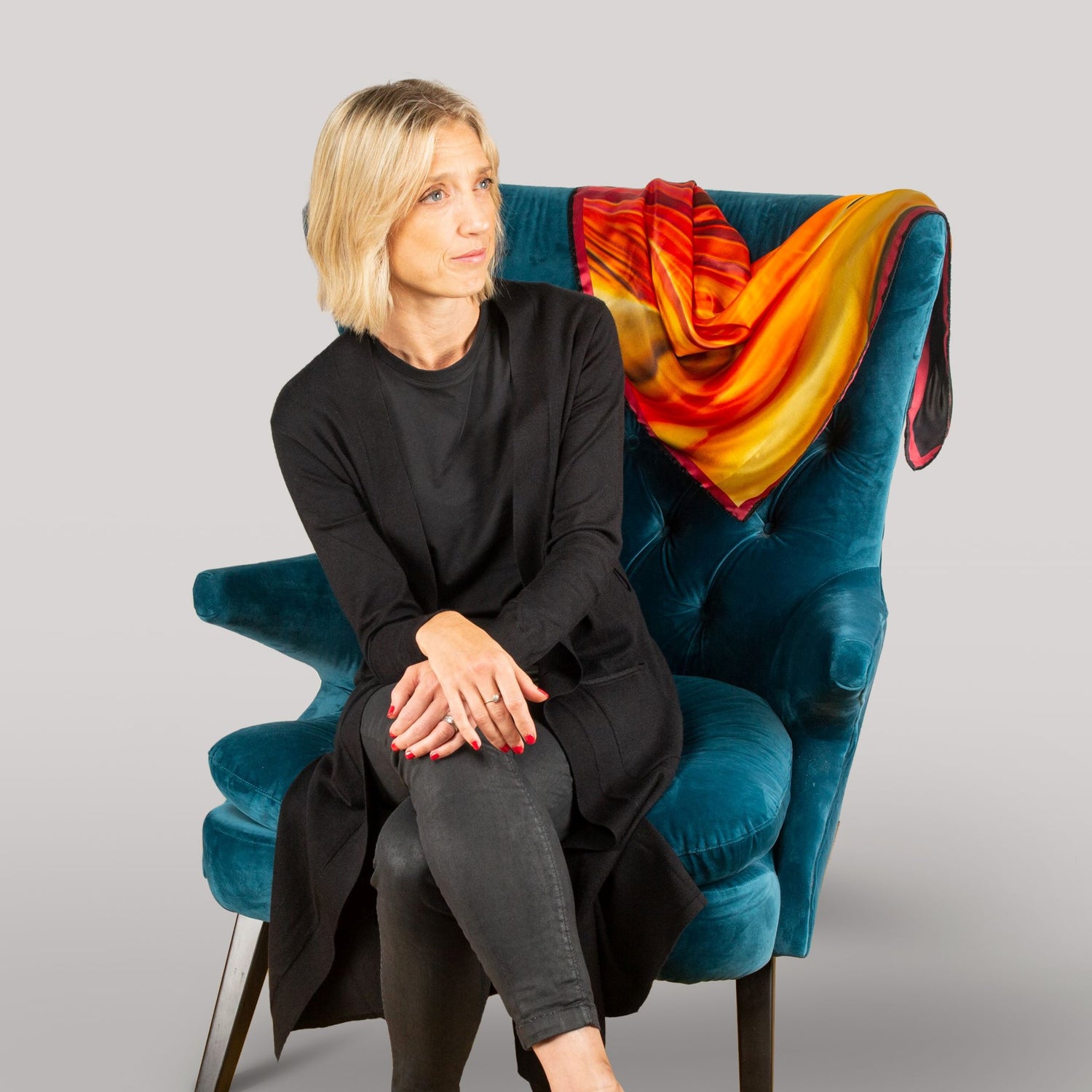 Siwan Oldham from By Biology sitting on armchair with a lava red silk scarf draped on the chair